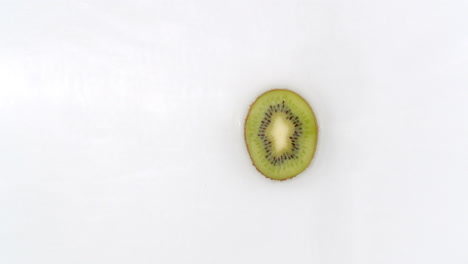 slow motion water splash on one slice of kiwi lying on a white background in water