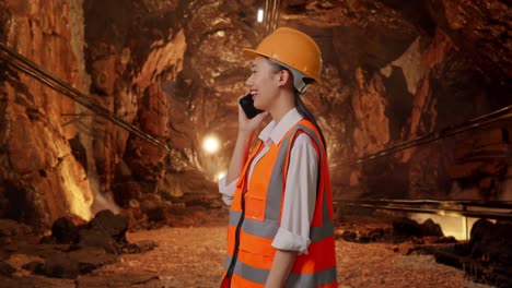 side view of asian female engineer with safety helmet talking on smartphone in underground mine tunnel