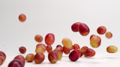 fresh red grapes off the vine falling and bouncing and rolling around on white table top in slow motion