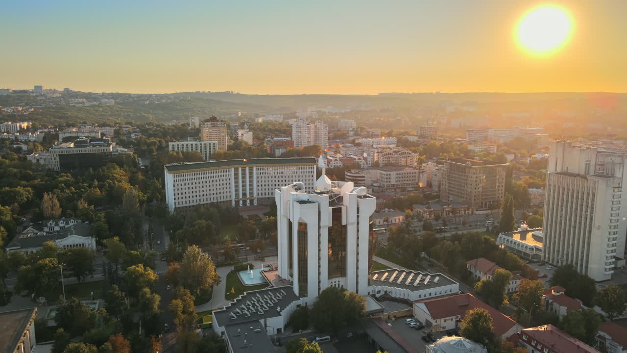 Aerial drone view of Chisinau downtown at sunset. Panorama view of multiple buildings, Parliament, Presidency, roads with moving cars and lush trees. Moldova