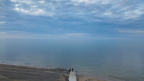 Slow-motion-altitude-shot-of-man-at-end-of-jetty-at-dusk-on-Fleetwood-Beach-Lancashire-UK