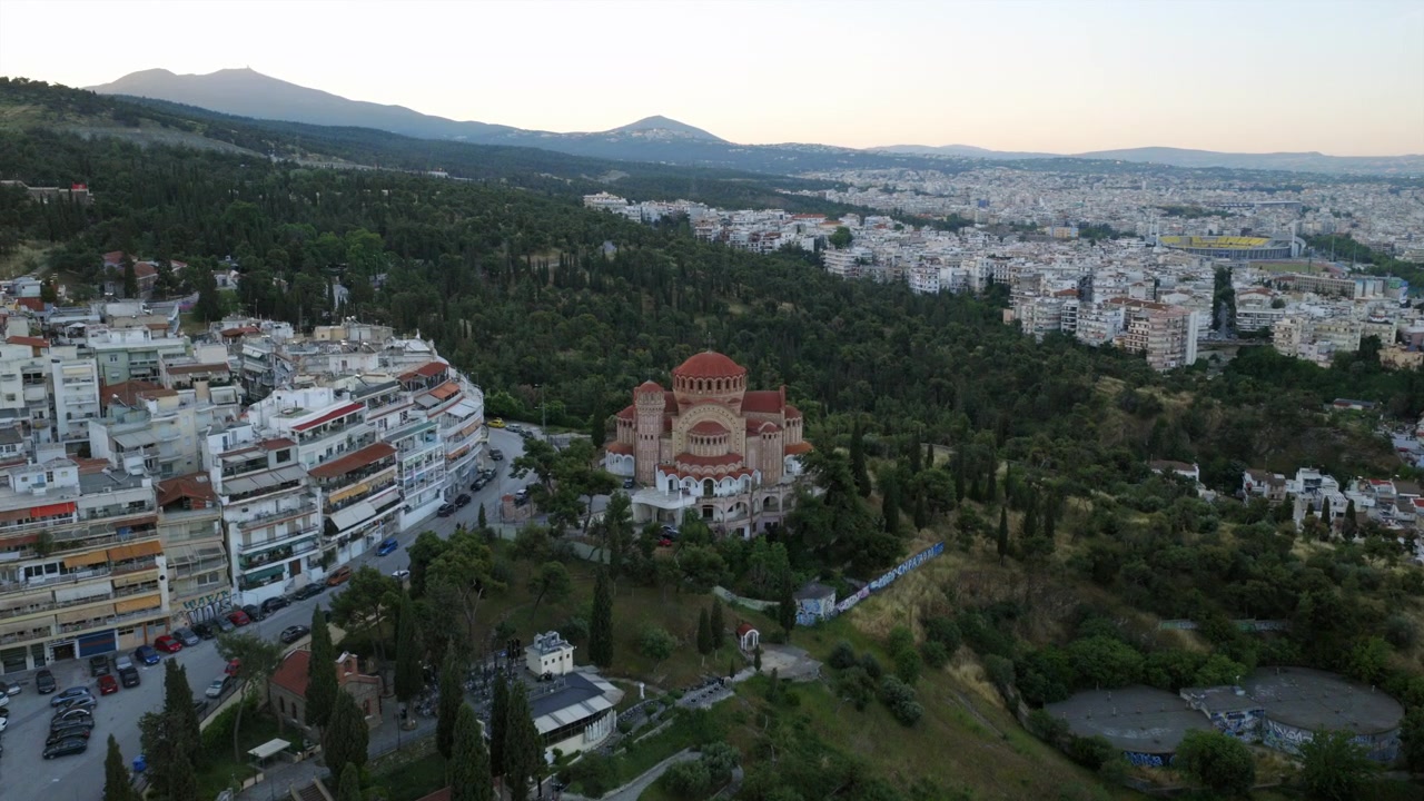 Vista aérea matutina con dron de la Iglesia de San Pablo en Tesalónica, Grecia, situada en una ladera verde con vistas a la extensa ciudad y a las montañas boscosas.