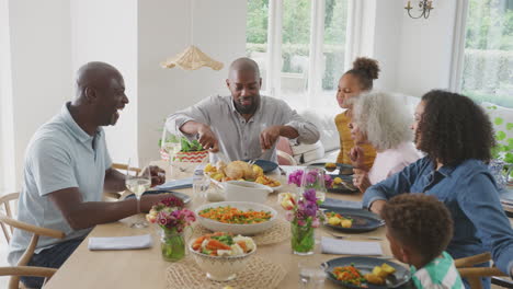 father carving as multi generation family sit around table at home and enjoy eating meal