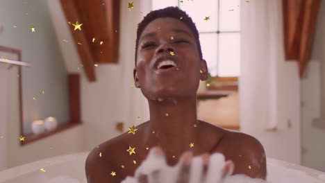 animation of gold stars falling over happy african american woman blowing foam in bath