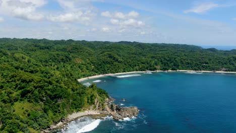 Pristine-Wediombo-beach,-Indonesia-surrounded-by-tropical-rain-forest,-aerial