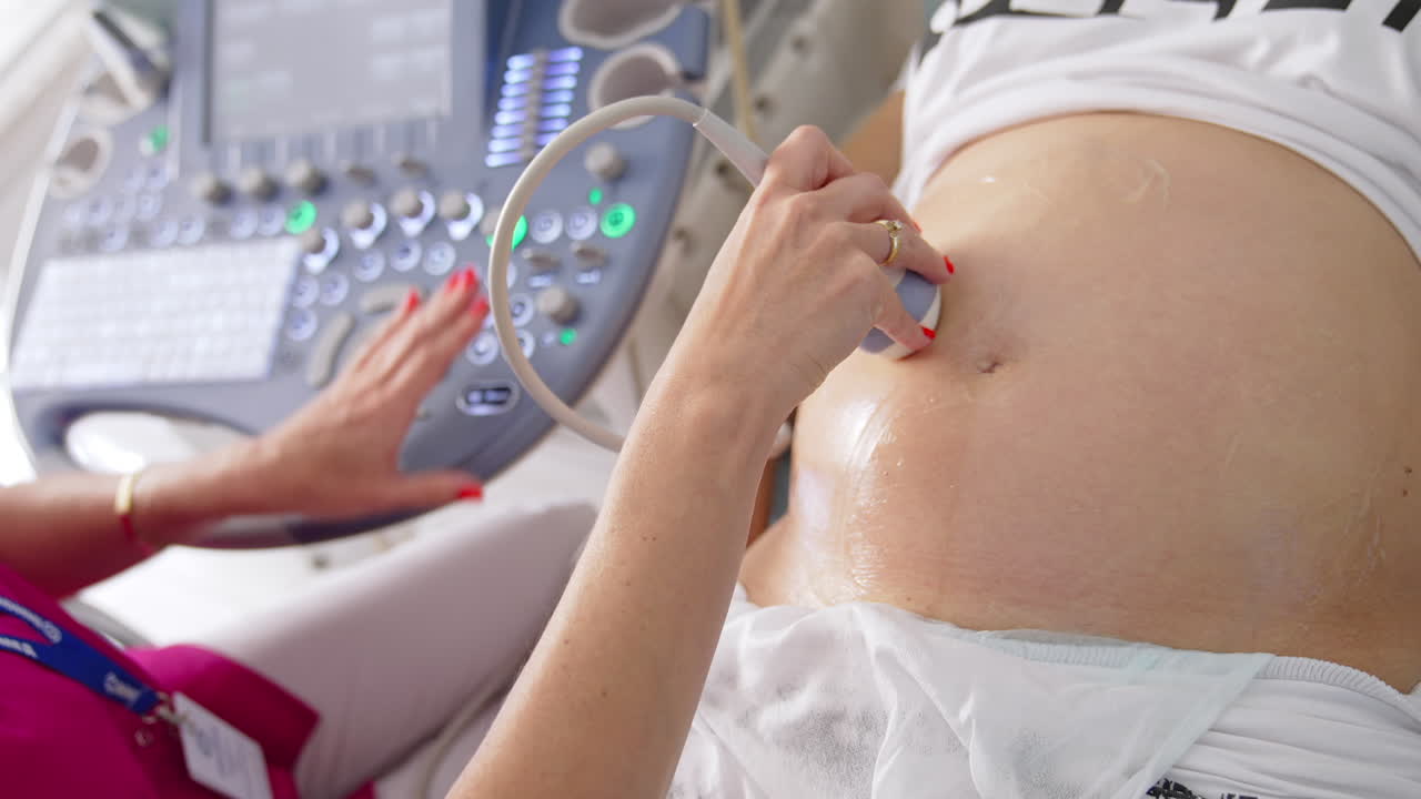 Doctor doing sonogram scan to a pregnant woman. Obstetrician moving transducer on the belly of the future mother. Modern medical equipment for ultrasound. Close-up.