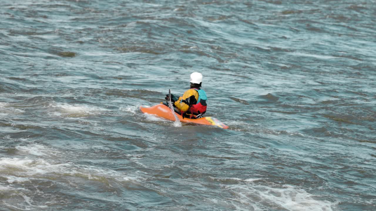 Kayaker con un kayak arancione che rema per posizionarsi e cavalcare la scia di un'onda sul fiume Ottawa
