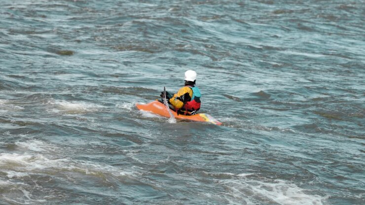 Kayaker con un kayak arancione che rema per posizionarsi e cavalcare la scia di un'onda sul fiume Ottawa