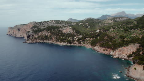 idyllic view of port de soller on sheer rock cliffs near deià with tramuntana mountains of mallorca, spain