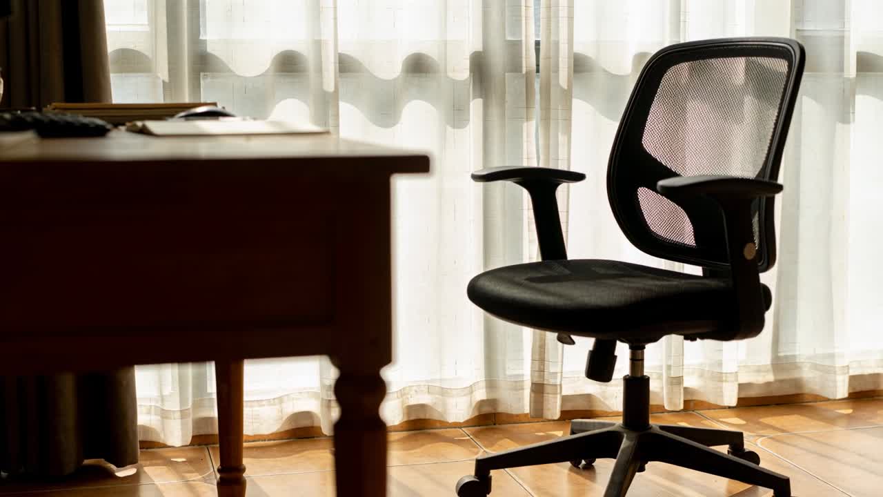 Una sedia girevole nera in rete ruota, muovendosi dopo un sottile spostamento della telecamera in un ufficio domestico, tra gli oggetti sulla scrivania.