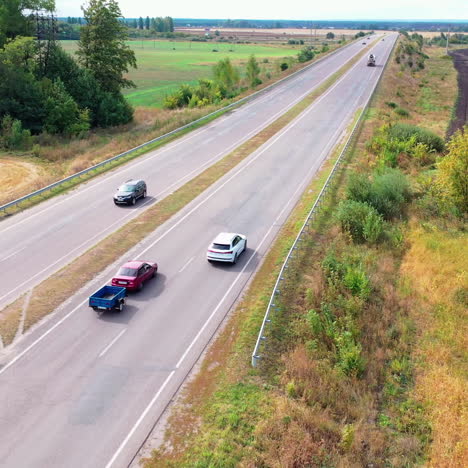 aerial view of a white car on highway. top view on the movement of cars on the road among fields and green trees background.