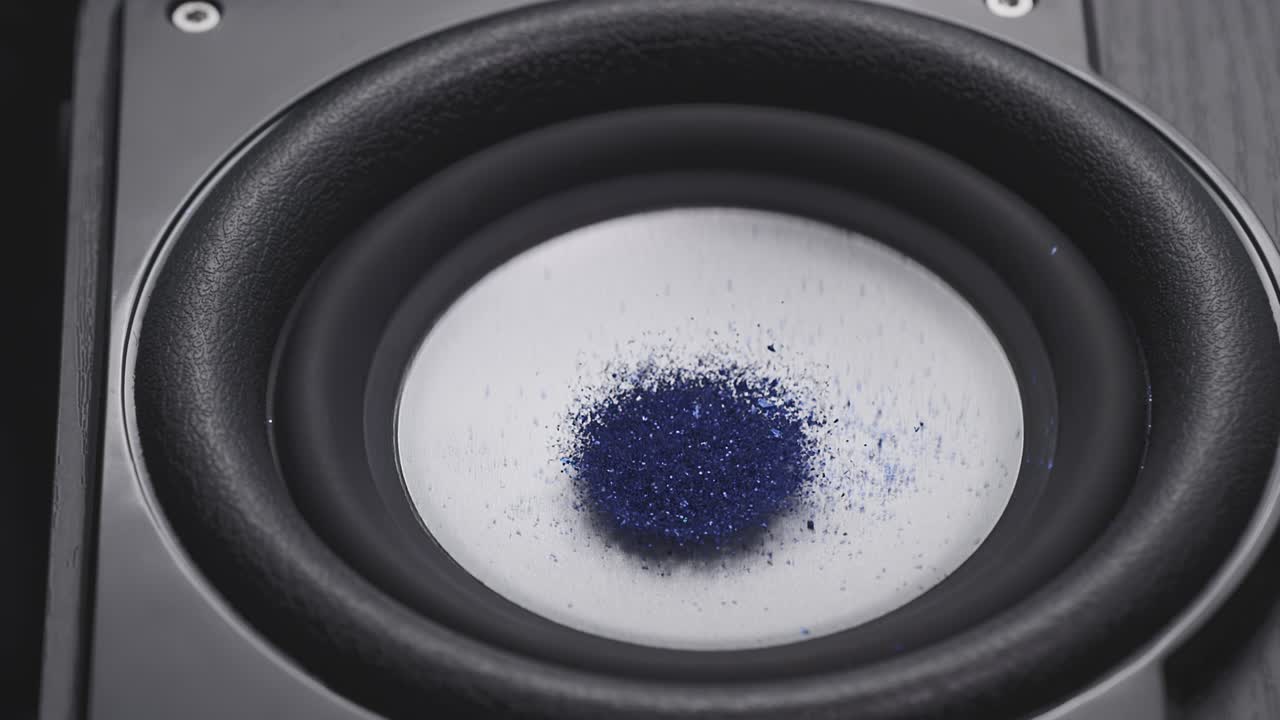 Trembling loudspeaker throwing orange dust in the air. Super slow motion close-up shot