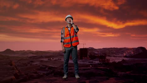 cuerpo lleno de ingeniero masculino asiático con casco de seguridad gritando con la mano sobre la boca mientras estaba de pie en el sitio de construcción, maquinaria de minería