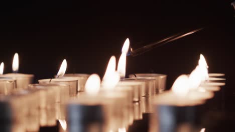 video of close up of rows of tea candles with white flames and copy space on black background