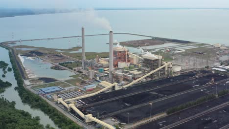 high angle pull out shot capturing large coalfield and industrial ultra-supercritical coal-fired power plant with smokes raising from chimney located at costal area of manjung, perak, malaysia