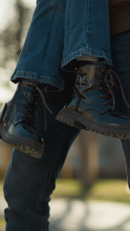 un hombre con una chaqueta marrón levanta a una chica que lleva vaqueros azules y botas negras. la escena captura un momento al aire libre con la luz del sol filtrándose a través de los árboles en el fondo