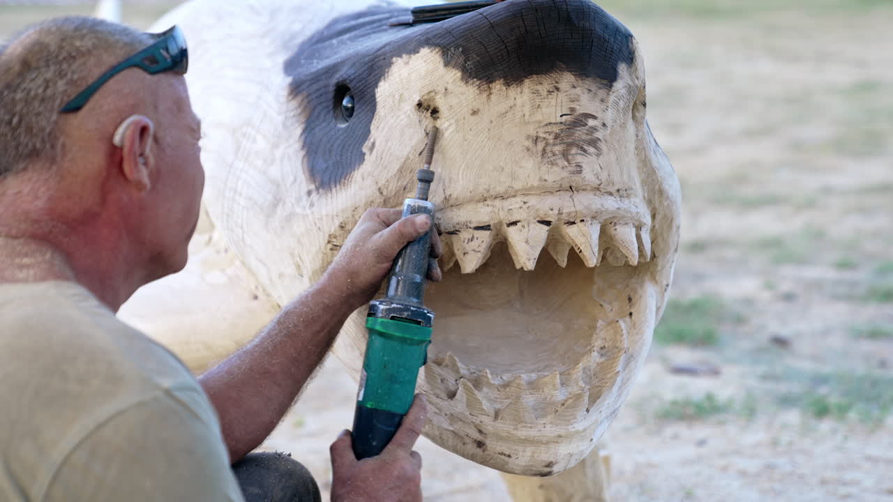 Wooden shark sculpture creation. Male artist uses electric tool to make the nostrils of the animal figurine.