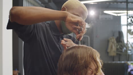 afro-american barber in mask brushing hair of man with comb