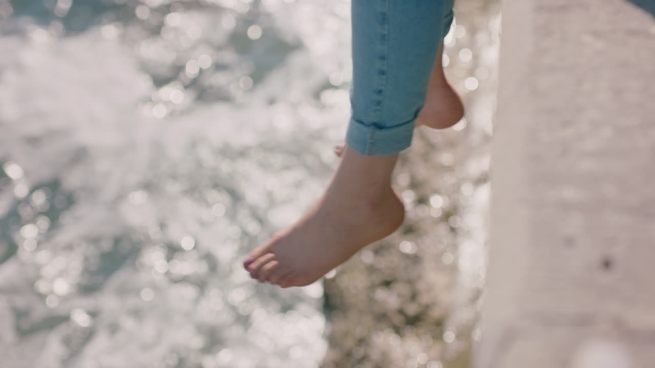 여자 다리가 물 위에 흔들리는 맨발 소녀가 여름 휴가를 즐기고 해변 기 ?? 에 앉아 파도를 지켜보는 자유 개념