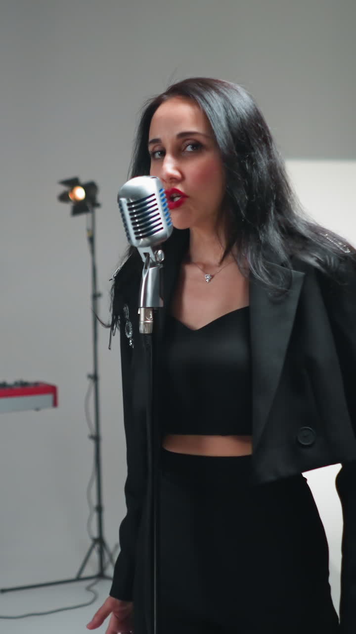 vocalista femenina emotiva en traje negro cantando apasionadamente con gestos de la mano, la cámara dinámicamente acercándose y alejándose sobre un fondo blanco