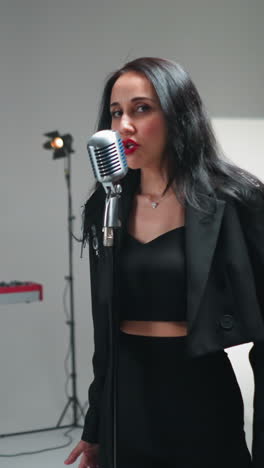 vocalista femenina emotiva en traje negro cantando apasionadamente con gestos de la mano, la cámara dinámicamente acercándose y alejándose sobre un fondo blanco