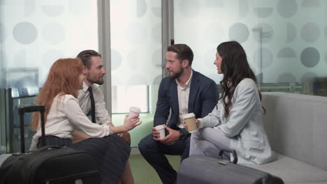 un grupo de trabajo de dos mujeres empresarias y dos hombres de negocios charlando relajadamente con unos cafés en el vestíbulo de un aeropuerto antes de un viaje de negocios