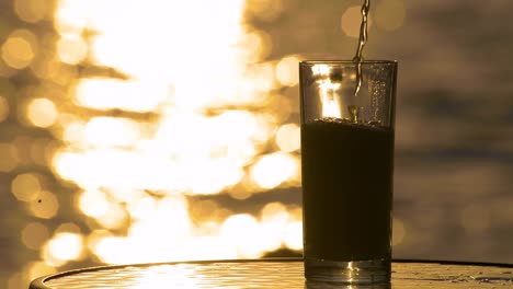 amber ale lager beer being poured into a glass with the sea and the sunset in the background