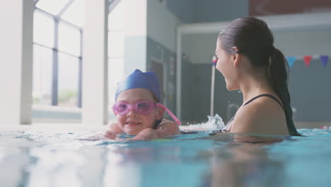 Schwimmtrainerin-Gibt-Mädchen,-Das-Schwimmunterricht-Im-Pool-Hält