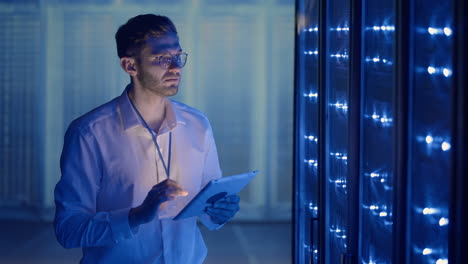 it technician in data center digital server room controlling work of rack server cabinets with a tablet. professional server engineer at work.