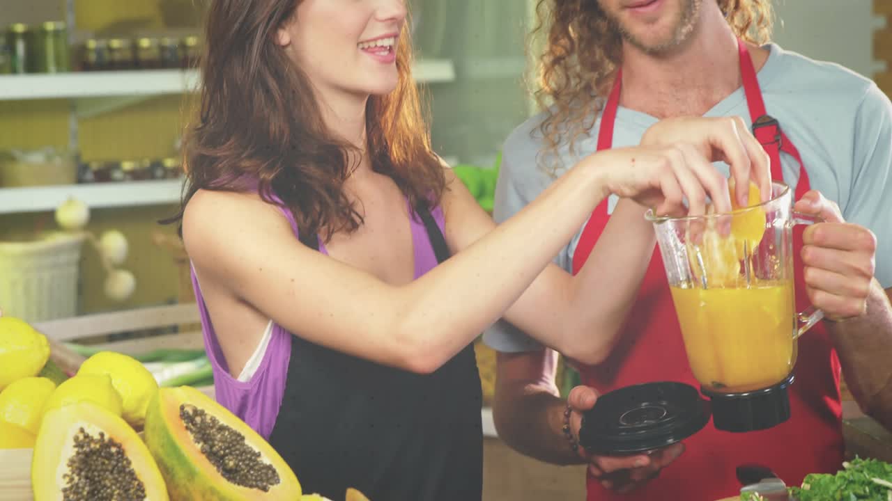 Woman reaching for blender and adding fruit while man placing lid to make juice, motion overlays