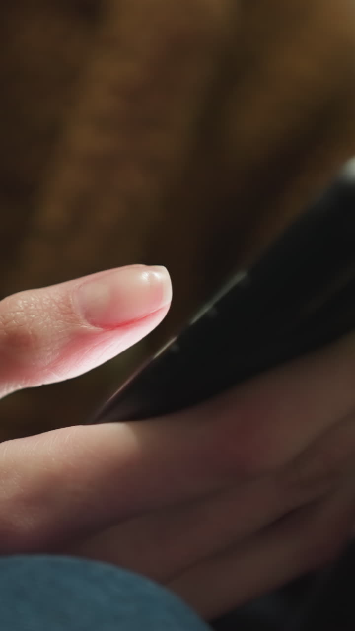 primer plano de una mano con un abrigo marrón y vaqueros azules, sosteniendo y desplazando un teléfono inteligente, los dedos interactuando con el dispositivo, capturando un momento de contemplación tranquila