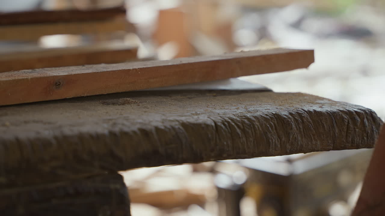 Sega a mano appoggiata su una tavola di legno pronta per il taglio, il bordo della lama che cattura la luce solare soffusa, venature testurizzate e trucioli fini su una superficie di lavoro ruvida, manico usurato e denti metallici a fuoco nitido, silenzioso.