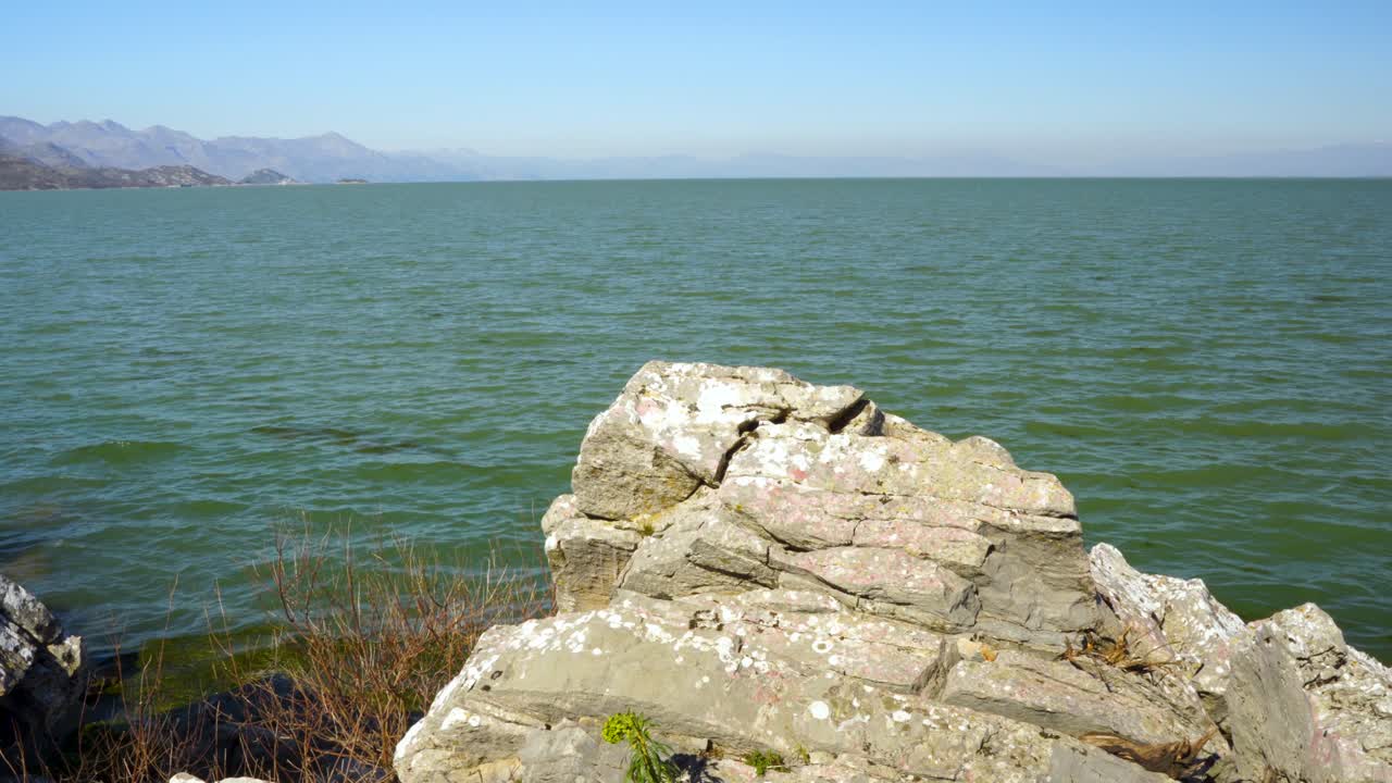 Old stones with beautiful shapes on rocky shore of mountain lake Scutari washed by vibrant water on a sunny day