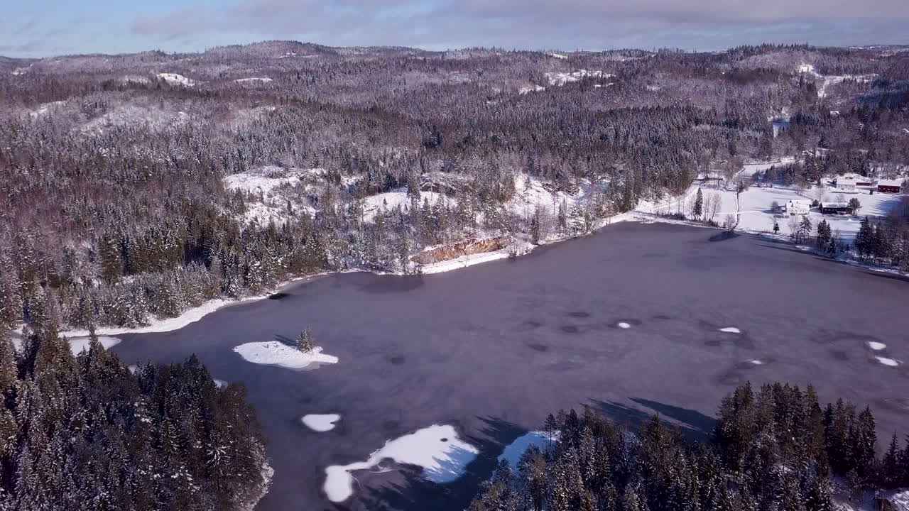 Flygfoto med drönare över en isig damm, kullar och skog, en solig vinterdag, i Risvann, Birkeland, Agder, södra Norge.