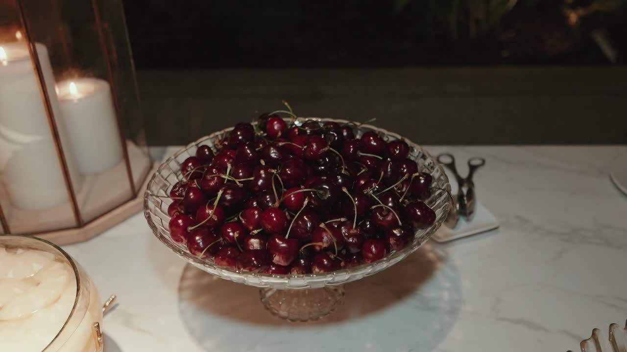 Ciotola di ciliegie rosse mature esposte in eleganti bicchieri su una superficie di marmo a lume di candela.