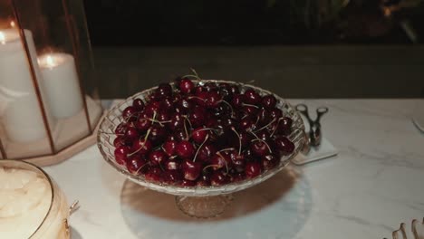 bowl of ripe red cherries displayed in elegant glassware on a marble surface with candlelight