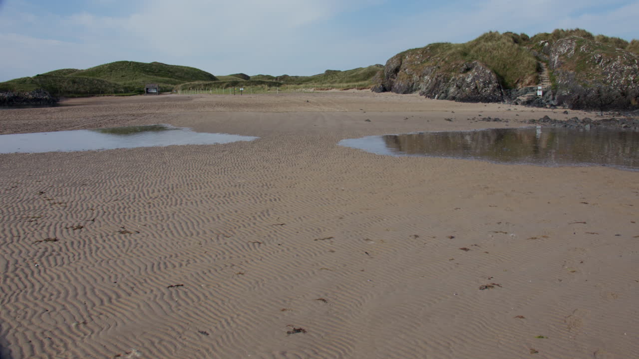 Timelapse Shot of the High tide coming in over dry sand and linking the Ynys Llanddwyn island