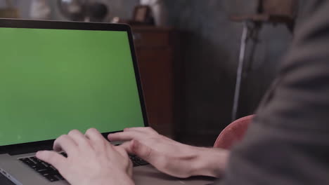 person typing on laptop with green screen