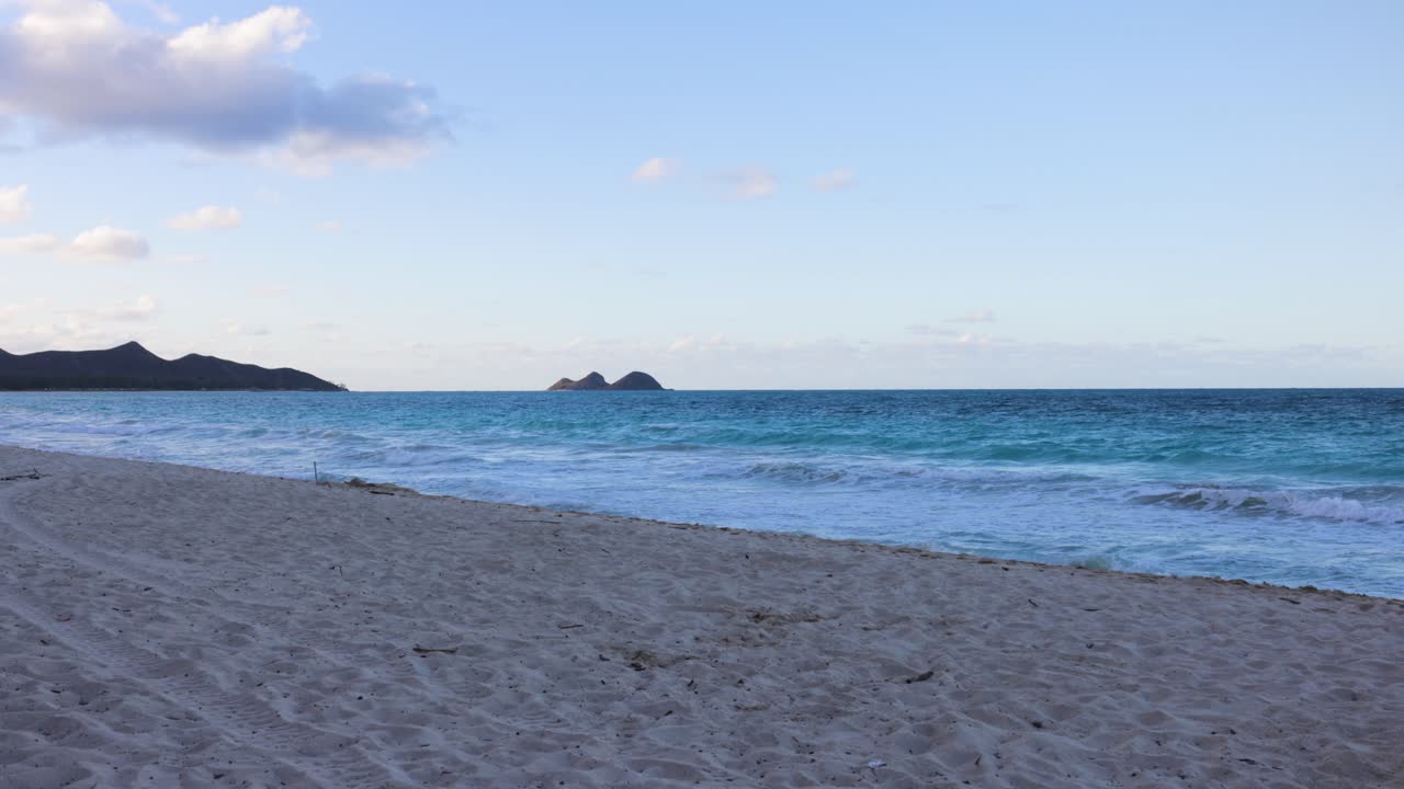 Piccole onde si infrangono su una tranquilla spiaggia sabbiosa con un cielo blu e nuvole bianche e gonfie
