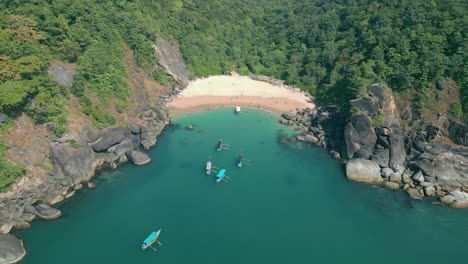 drone view of butterfly beach in goa, india, boats lined along the shore with lush green forest forming a vibrant backdrop 4k