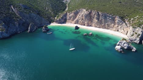 aerial descending fly-by of a yacht mooring at a tropical turquoise beach in portugal