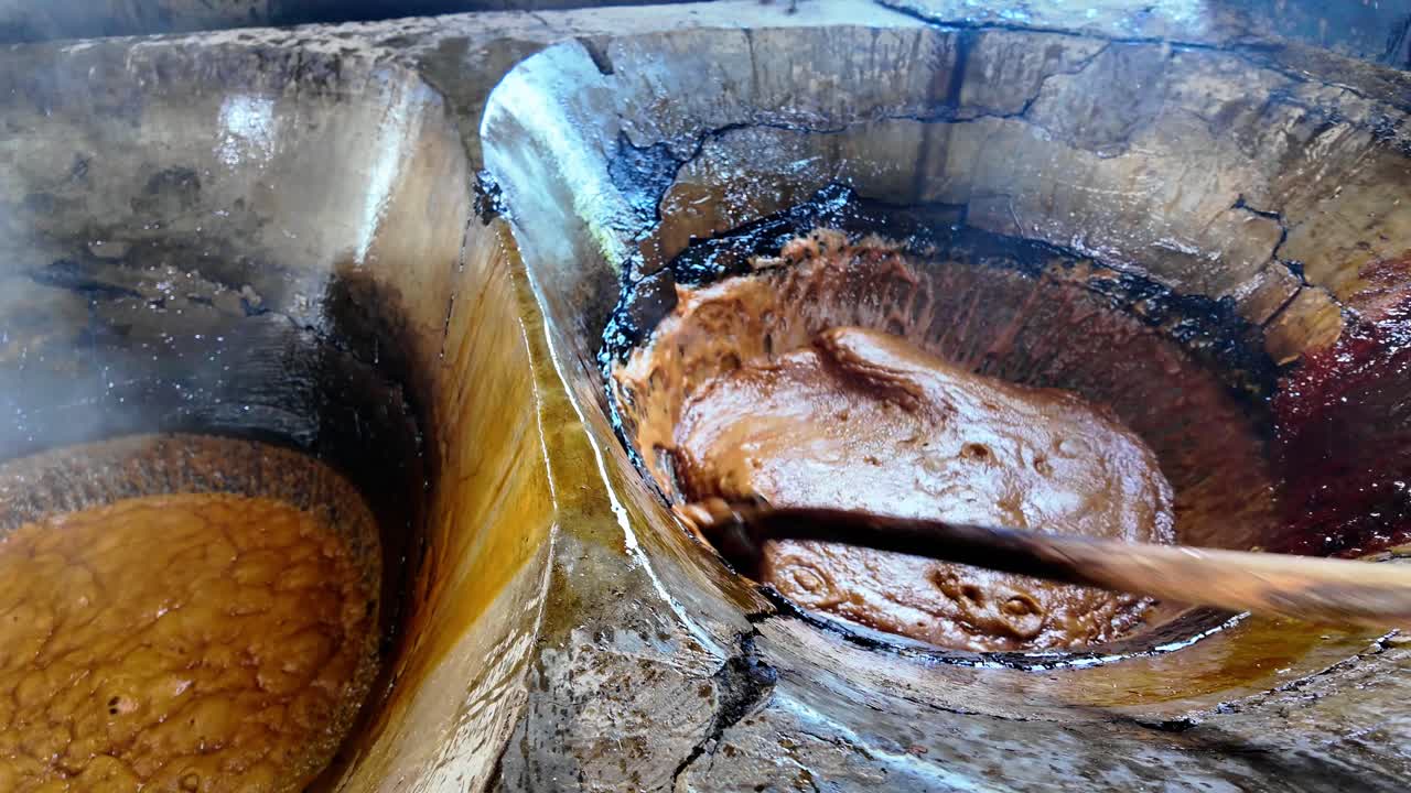 Man stirs a pot of hot caramelized sugar in a large vat for candy making