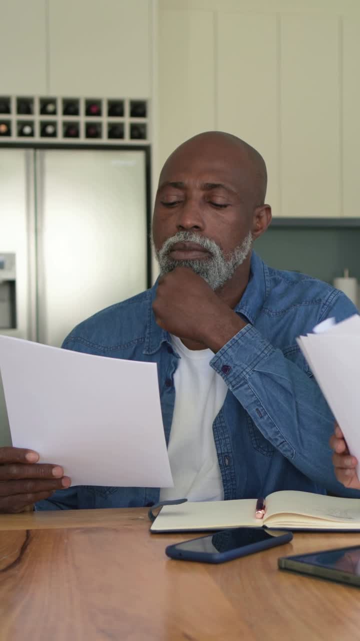 Vertical video: Reading man in denim reviewing papers at home table talking as partner handing more