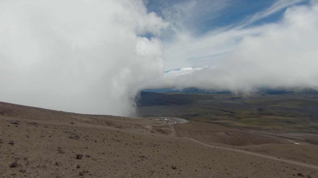 Establishing overview of rocky dry slopes Cotopaxi volcano, Ecuador, framed by a deep blue sky and rugged volcanic slopes as mist clouds roll in