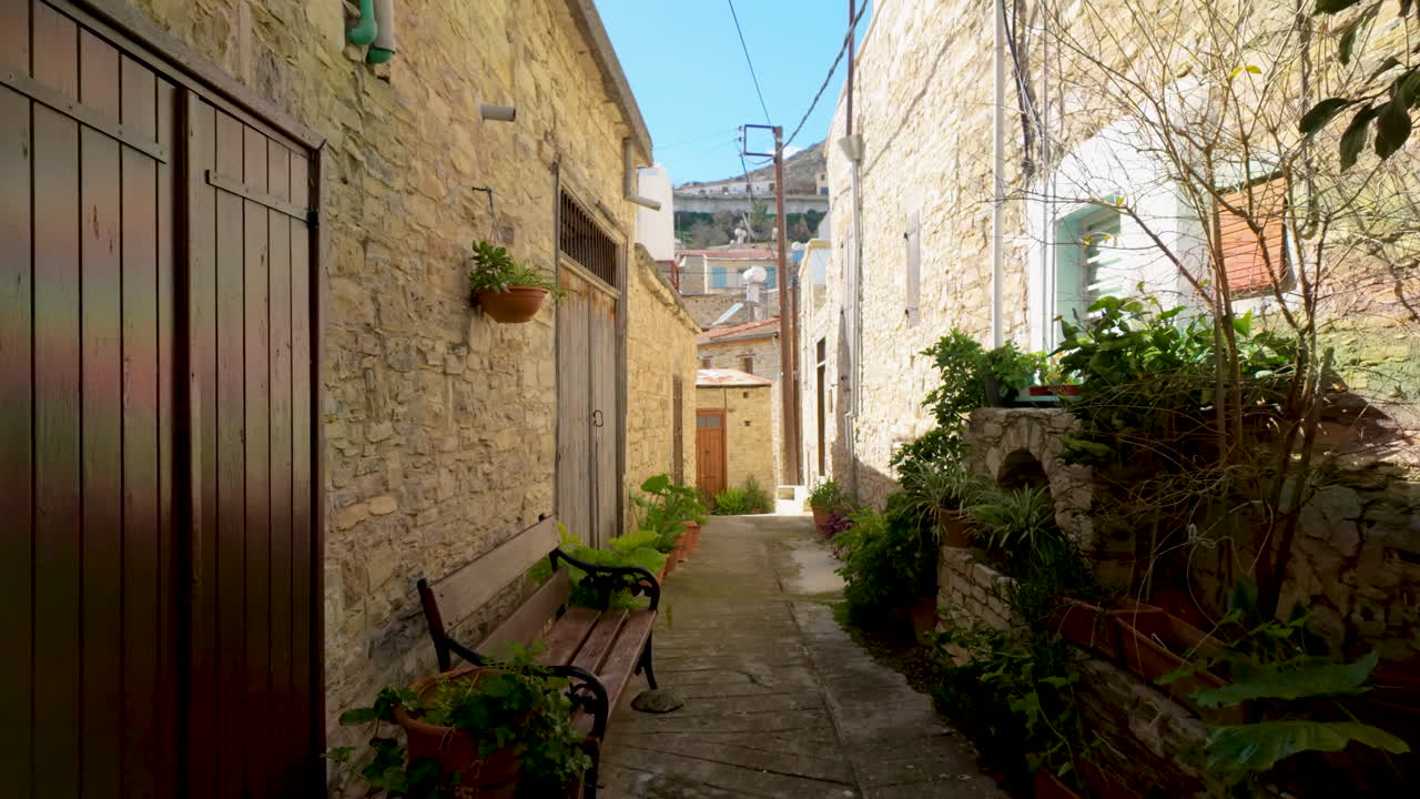 Un tradizionale vicolo in pietra a Lefkara fiancheggiato da piante in vaso e panchine, che invita a una piacevole passeggiata per il villaggio