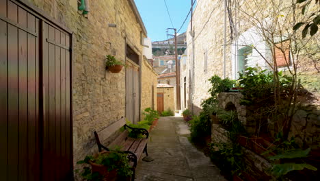 A-traditional-stone-alley-in-Lefkara-lined-with-potted-plants-and-benches,-inviting-a-leisurely-stroll-through-the-village