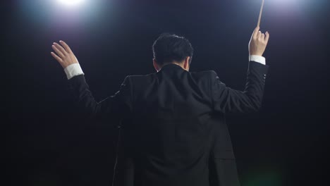 back view of asian conductor man holding a baton and showing gesture in the black studio