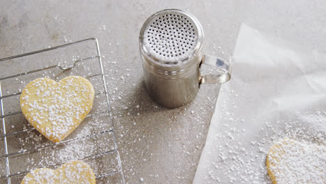 galletas en forma de corazón crudas en la bandeja de horneado con filtro de batidor de harina, cortador de galletas y papel de cera 4k