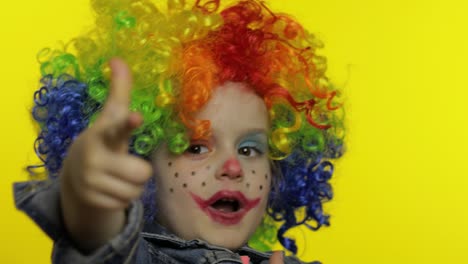 niña pequeña payaso en peluca haciendo caras tontas, tonto alrededor, muestra pistolas con las manos. halloween