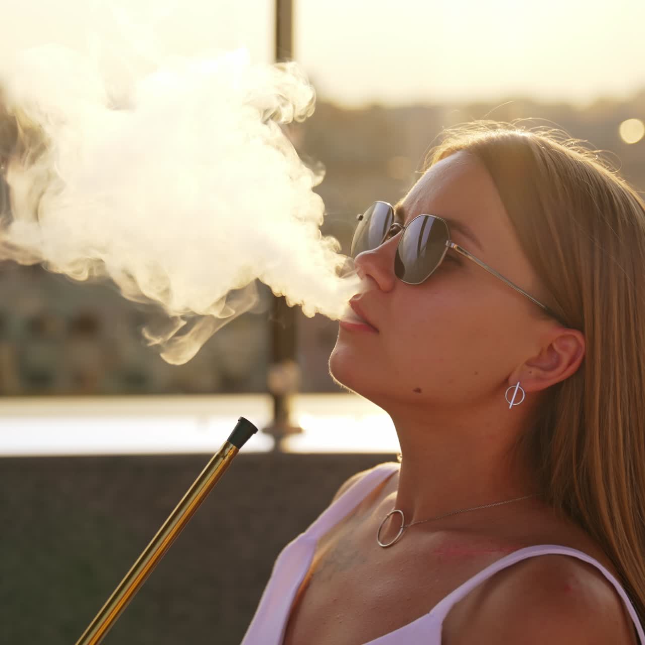 Smoking hookah in a café. Young long-haired woman breathes in and out thick white smoke. Close up. Blurred backdrop